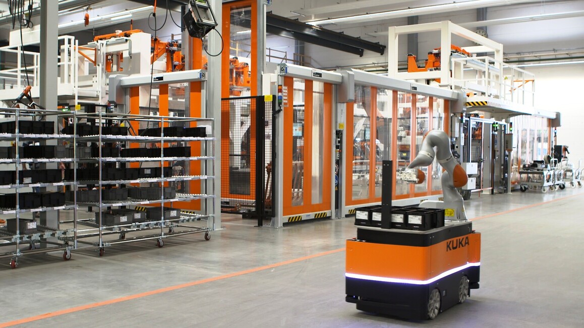 Ein Industrieroboter in einer Arbeitshalle mit Hochregalen.